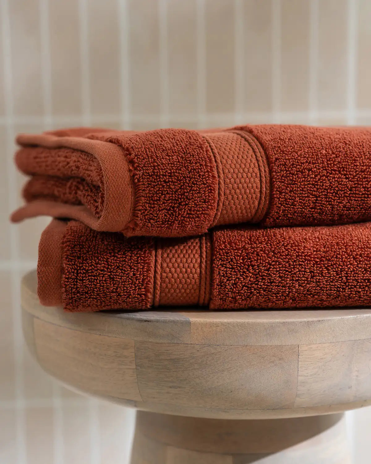 Stack of sienna modal cotton hand towels on a wooden stand with a neutral background