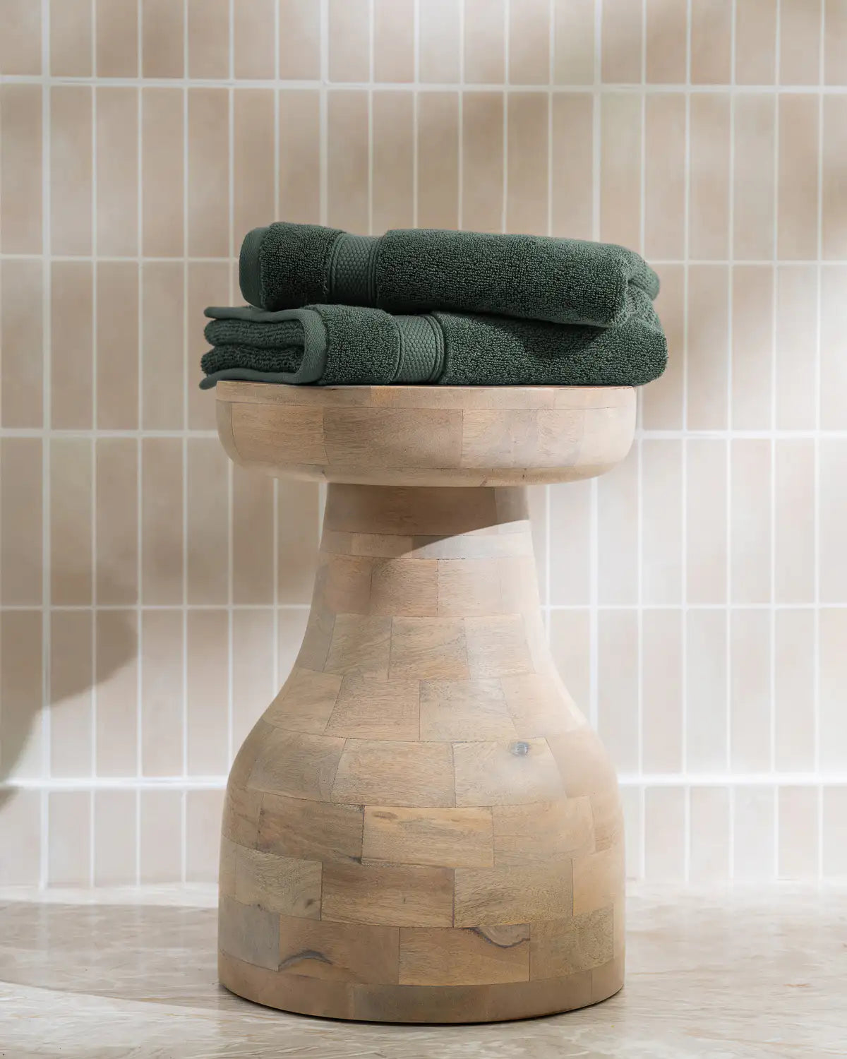 Wooden stool with pine green modal cotton washcloth towels on a tiled bathroom floor