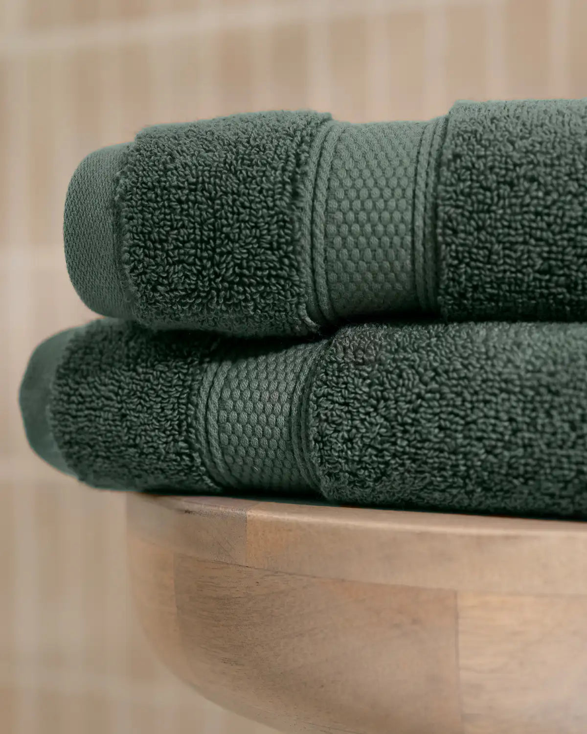 Two pine green modal cotton premium towels stacked on a wooden surface