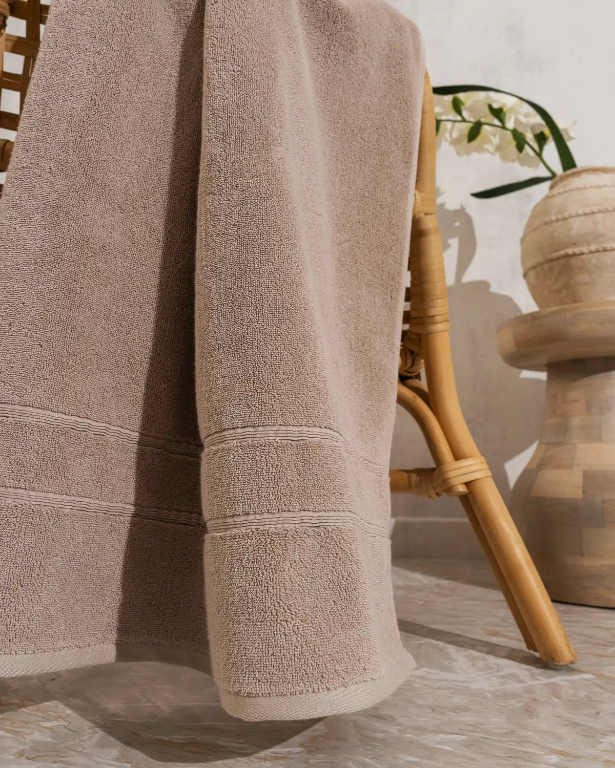 Sandshell classic Turkish cotton towel draped over a chair with a wooden table and plant in the background