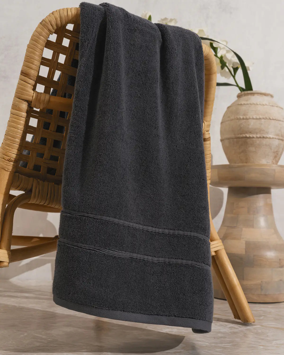 Dark tornado gray classic Turkish Bath towel draped over a wicker chair with a neutral background
