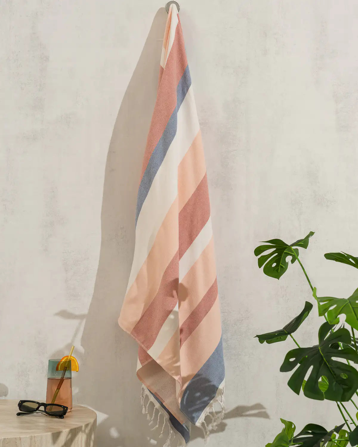 Soft Gradient Striped Beach & Pool Towel hanging on a wall with a plant and small table in the foreground
