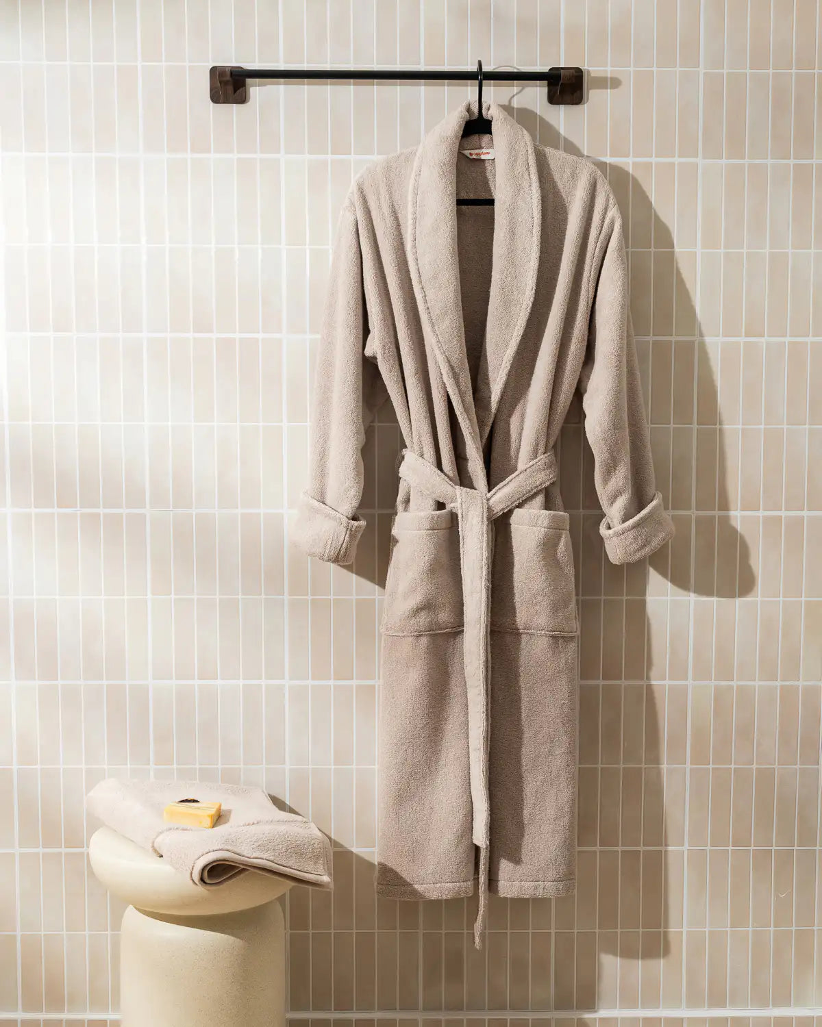 Sandshell ultrasoft bathrobe hanging on a rack against a tiled wall.