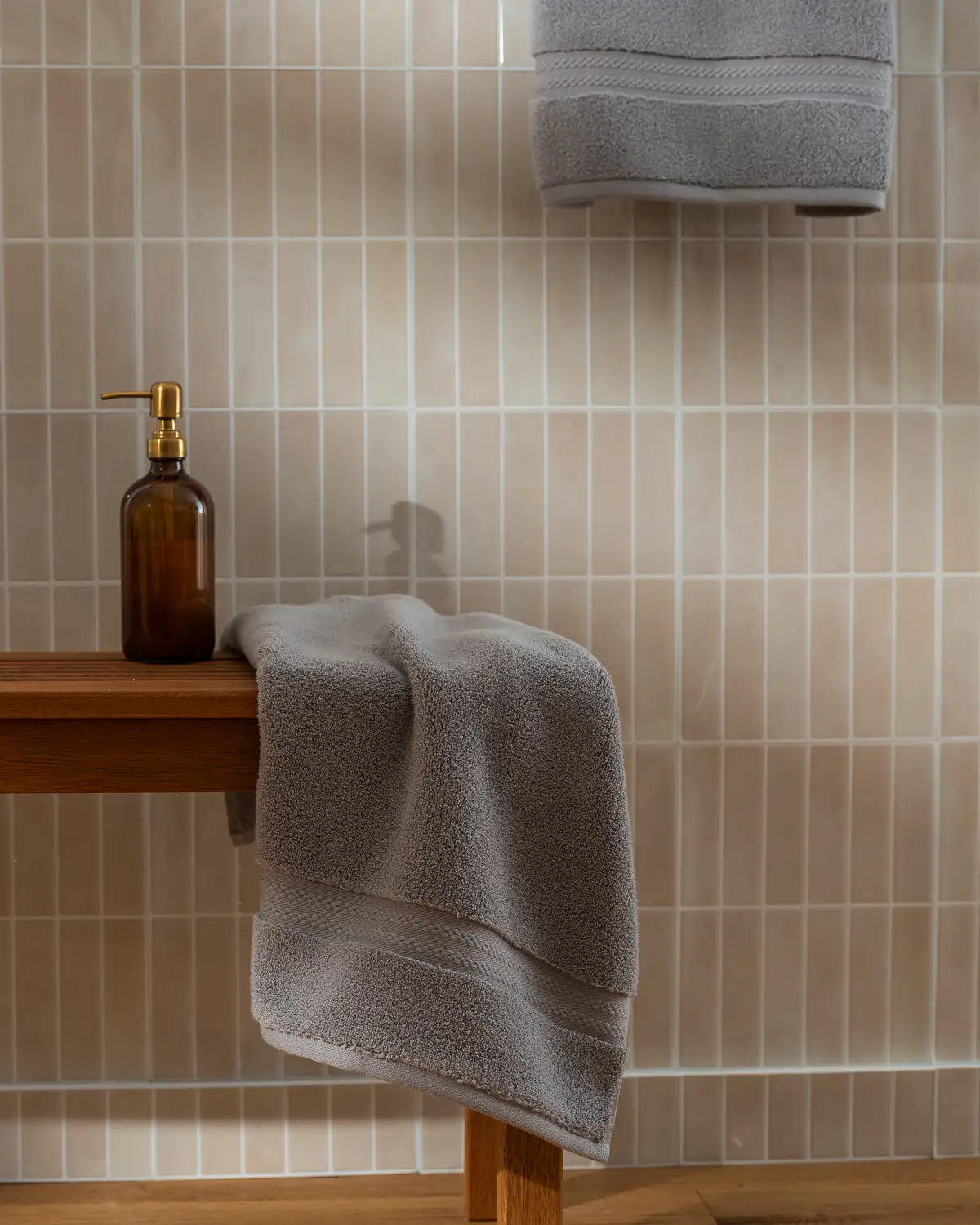 Gray towel draped over a wooden bench against a tiled bathroom wall.