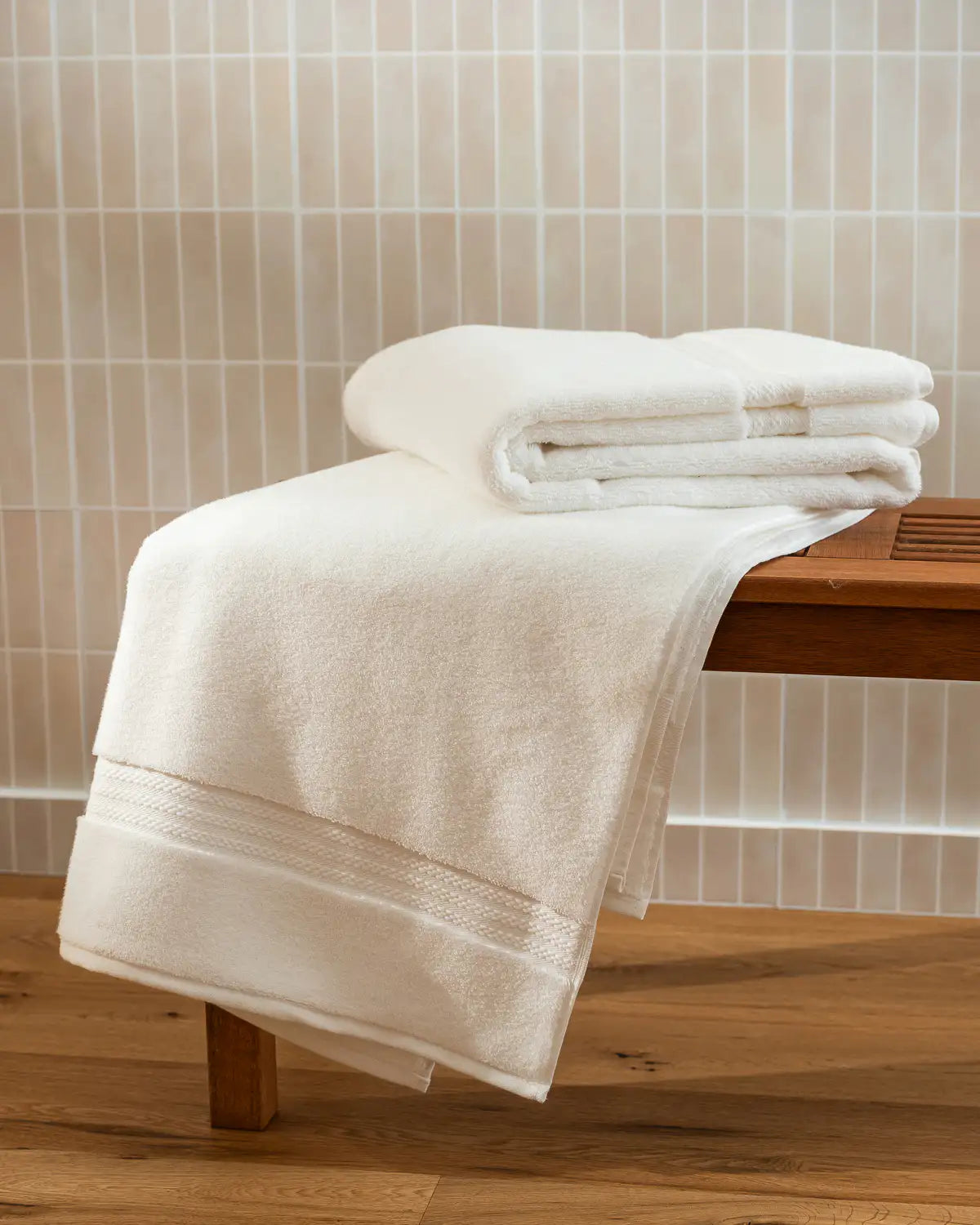White ultrasoft premium cotton towels on a wooden surface with a tiled wall background