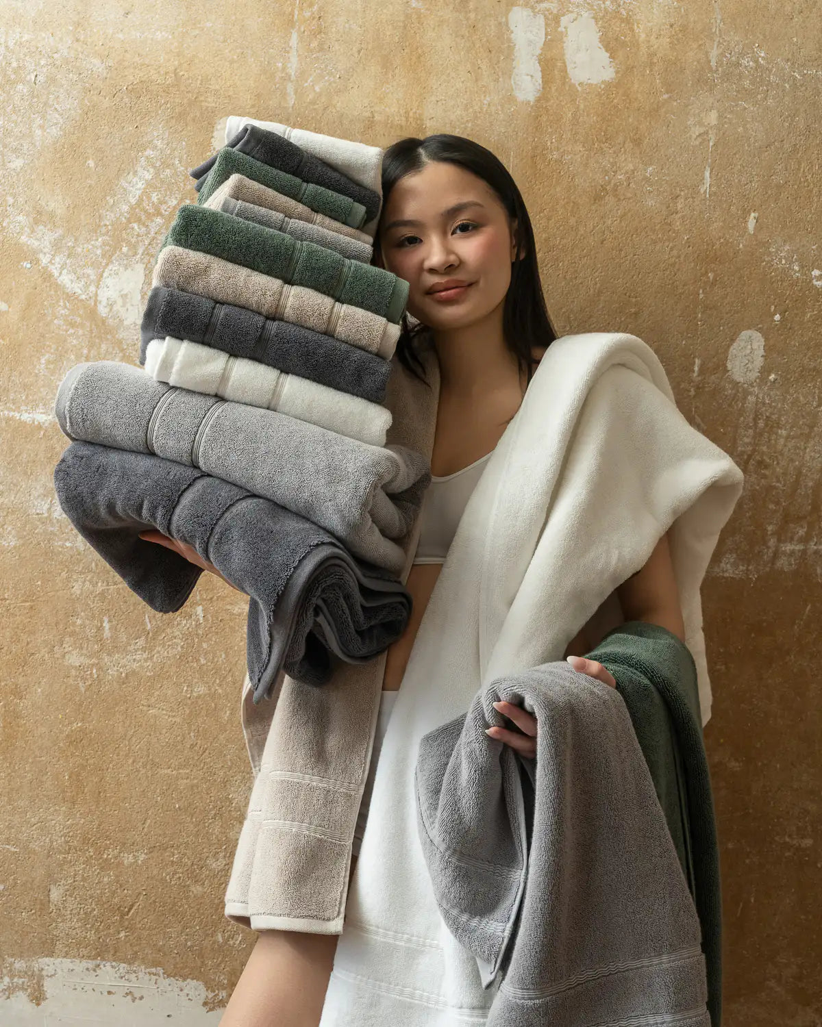 Woman holding a stack of folded classic Turkish towels against a textured beige wall