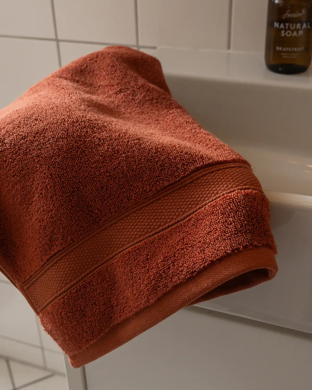 Sienna modal cotton premium towel draped over a bathtub with a bottle of soap in the background