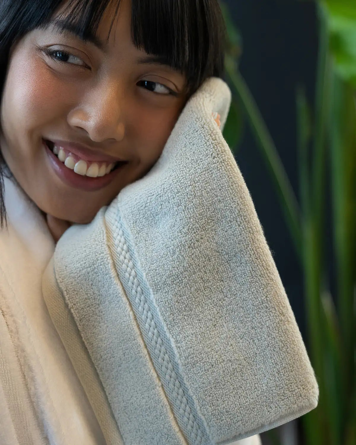 Person holding a jade ultrasoft cotton washcloth against their face with a blurred green background