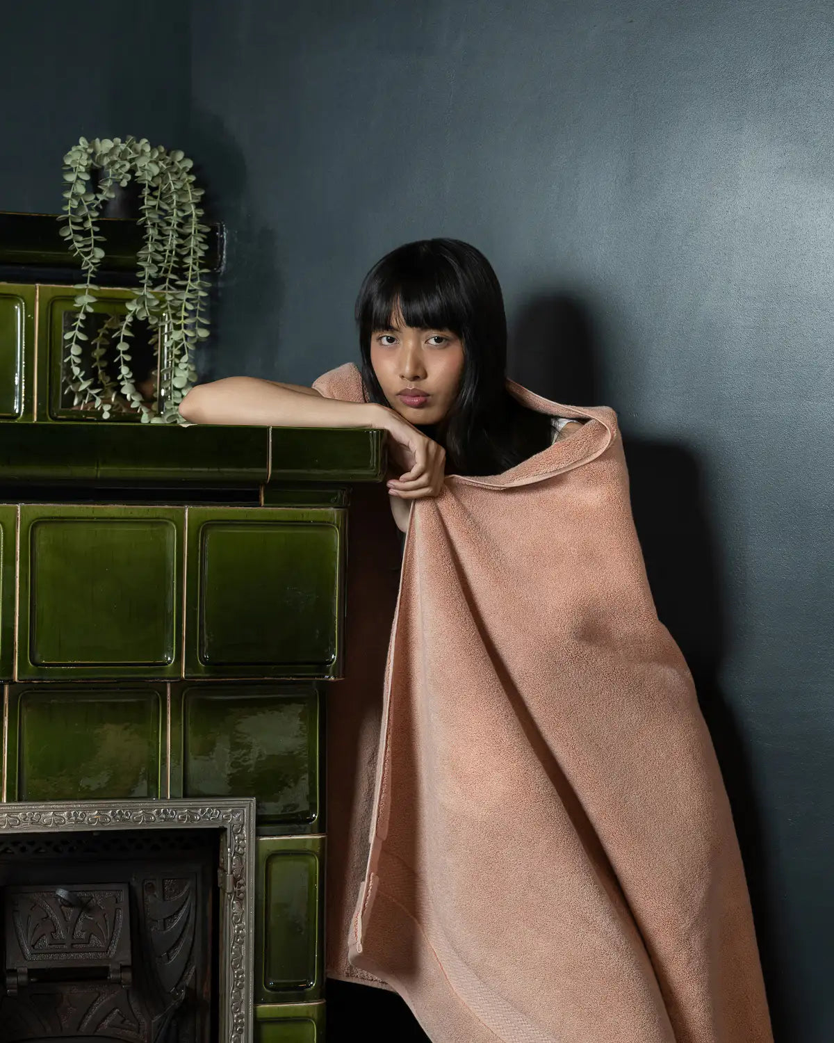 Woman wrapped in aalmond apricot ultrasoft premium cotton bath sheet leaning against a dark wall with green tiles.