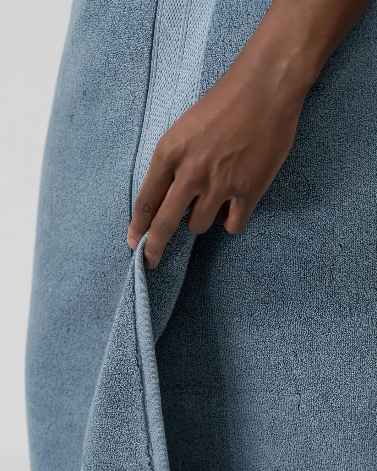 Hand holding a blue modal cotton bath sheet towel against a white background
