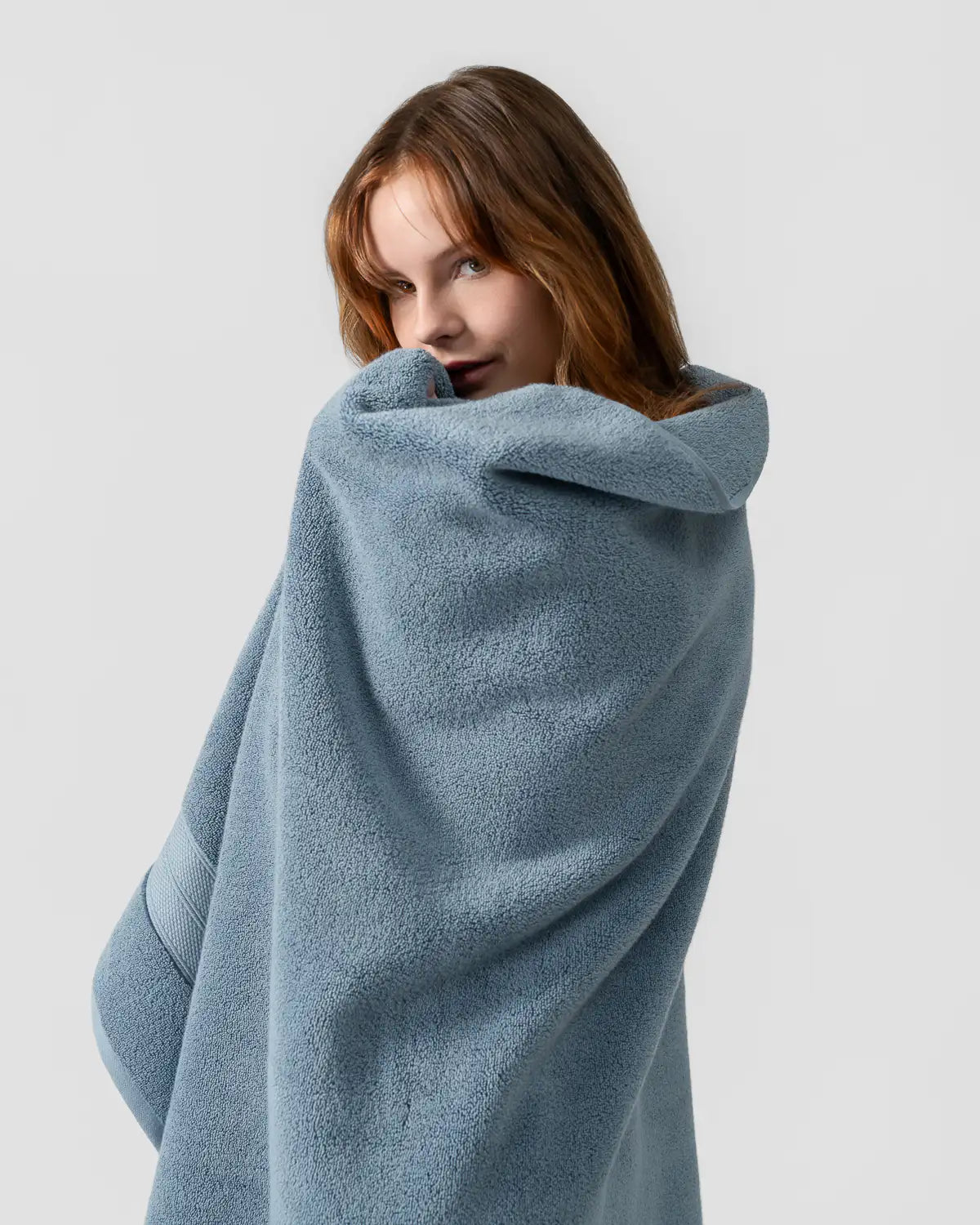 Woman wrapped in a blue shadow modal cotton towel against a light gray background