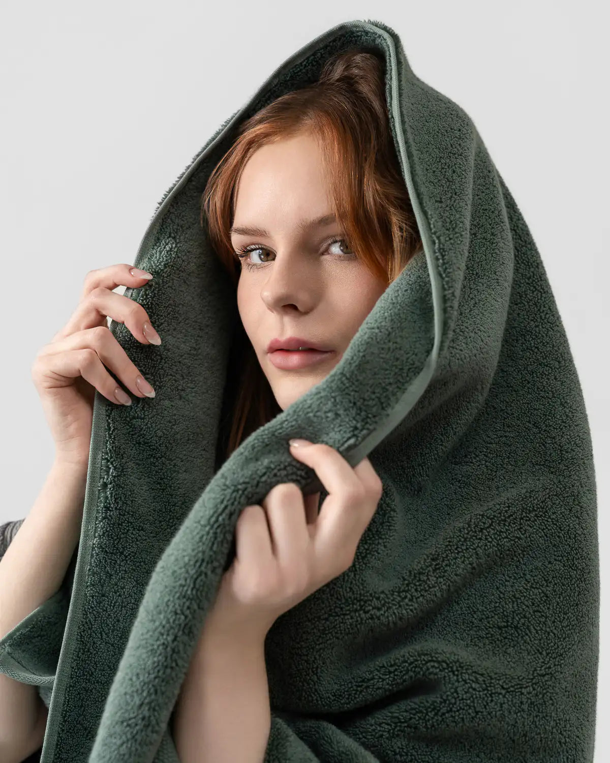 Person wrapped in a dark green towel against a light gray background