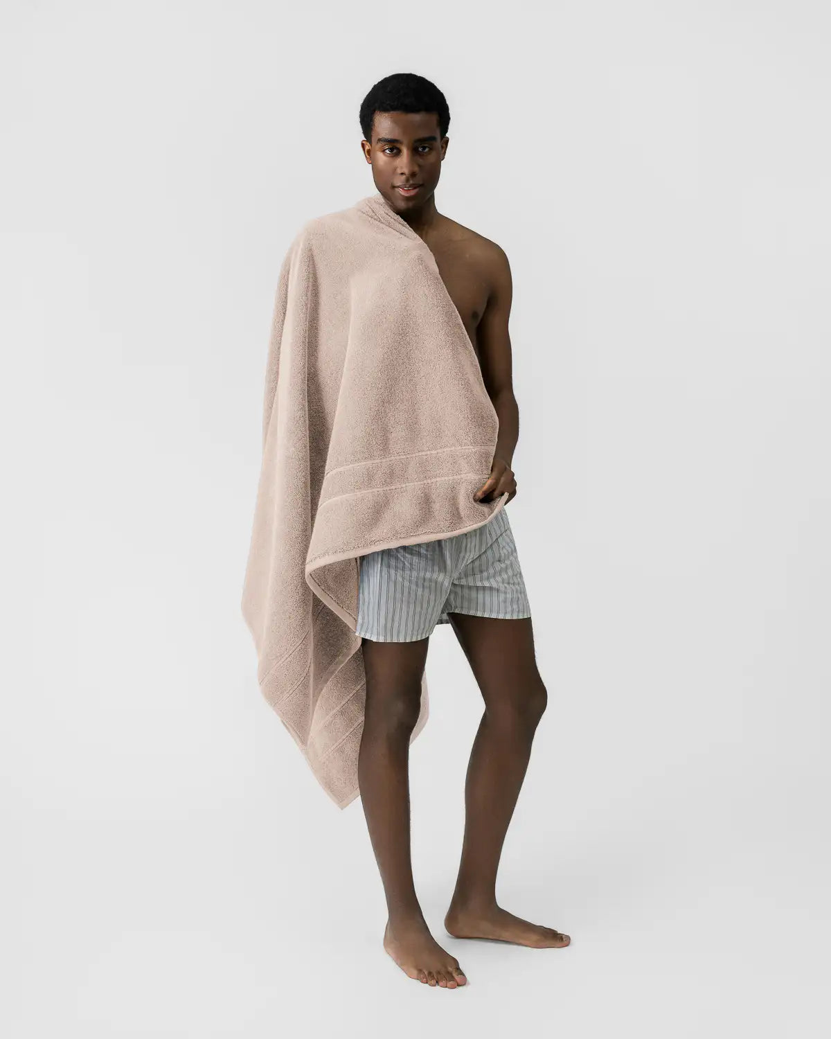 Person wrapped in a sandshell classic Turkish bath sheet on a plain background
