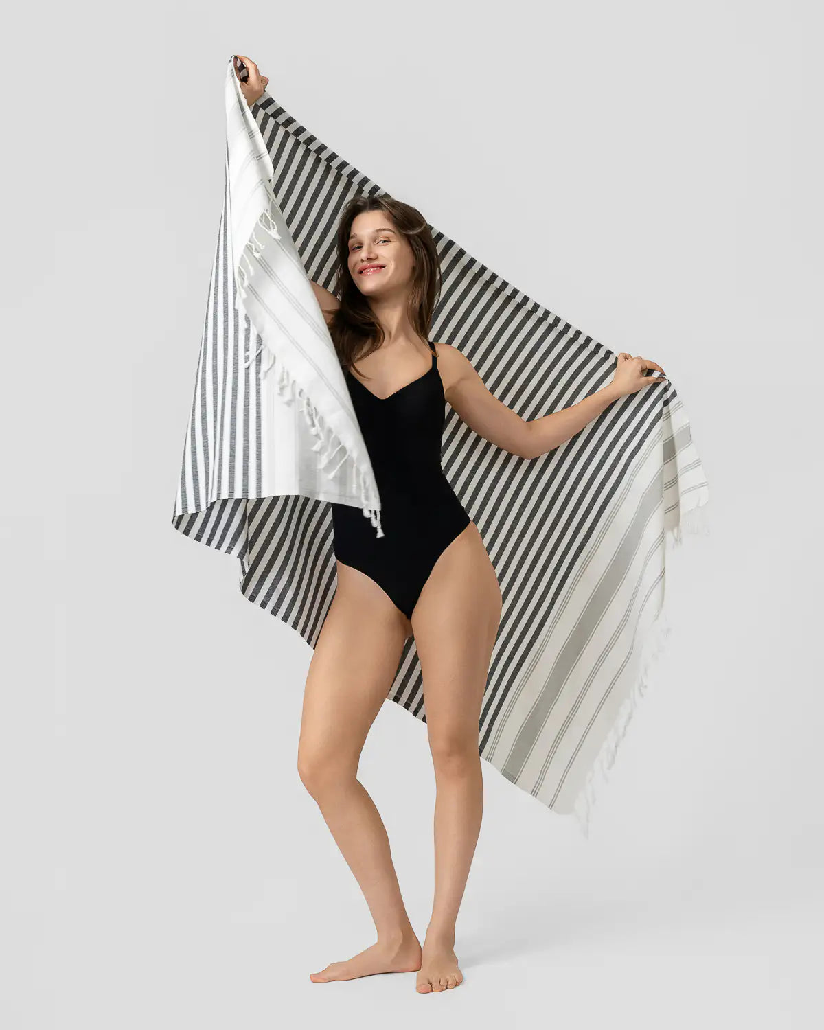 Woman holding a Ultra-Lightweight Multi-Purpose Beach Towel over her shoulders against a light gray background