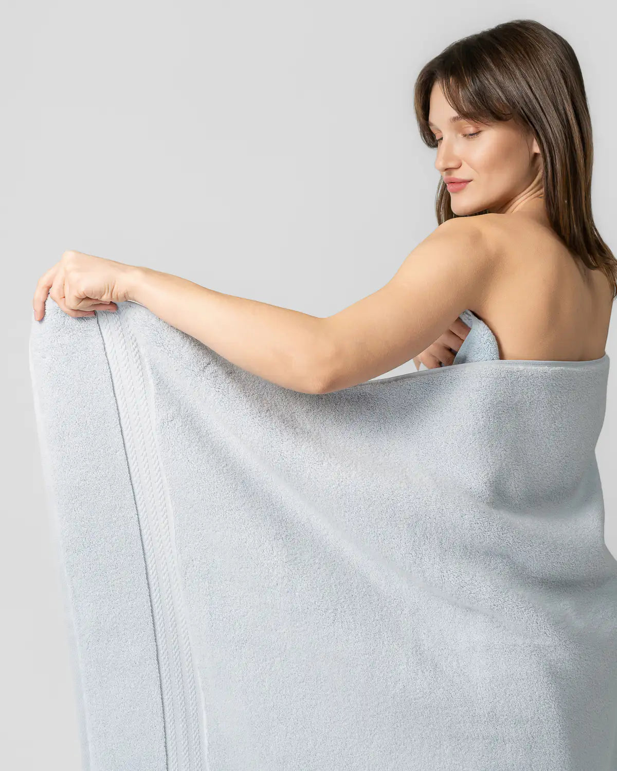 Woman holding a sky blue ultrasoft cotton towel against a plain background