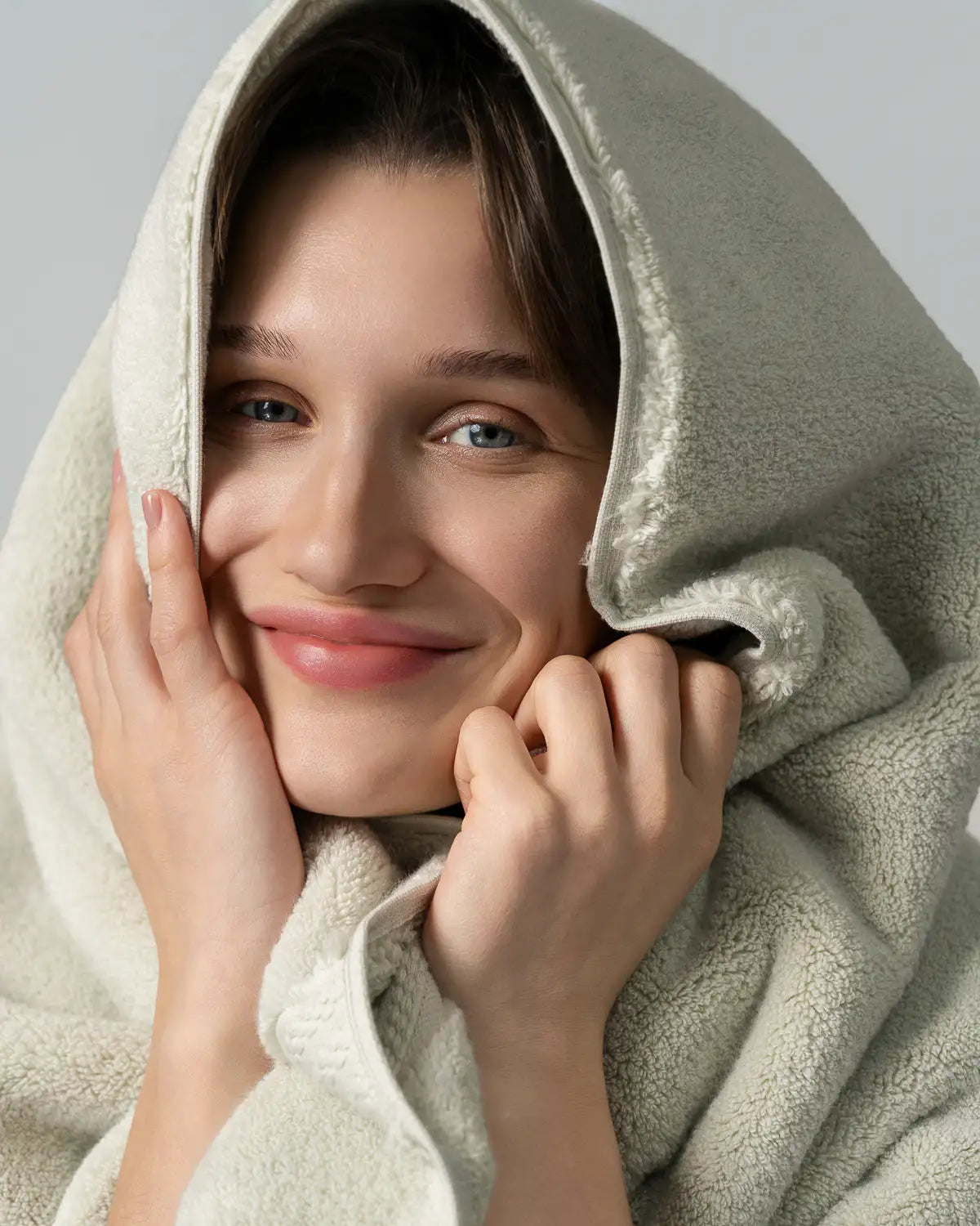 Woman wrapped in a jade ultrasoft cotton towel, smiling with a neutral background