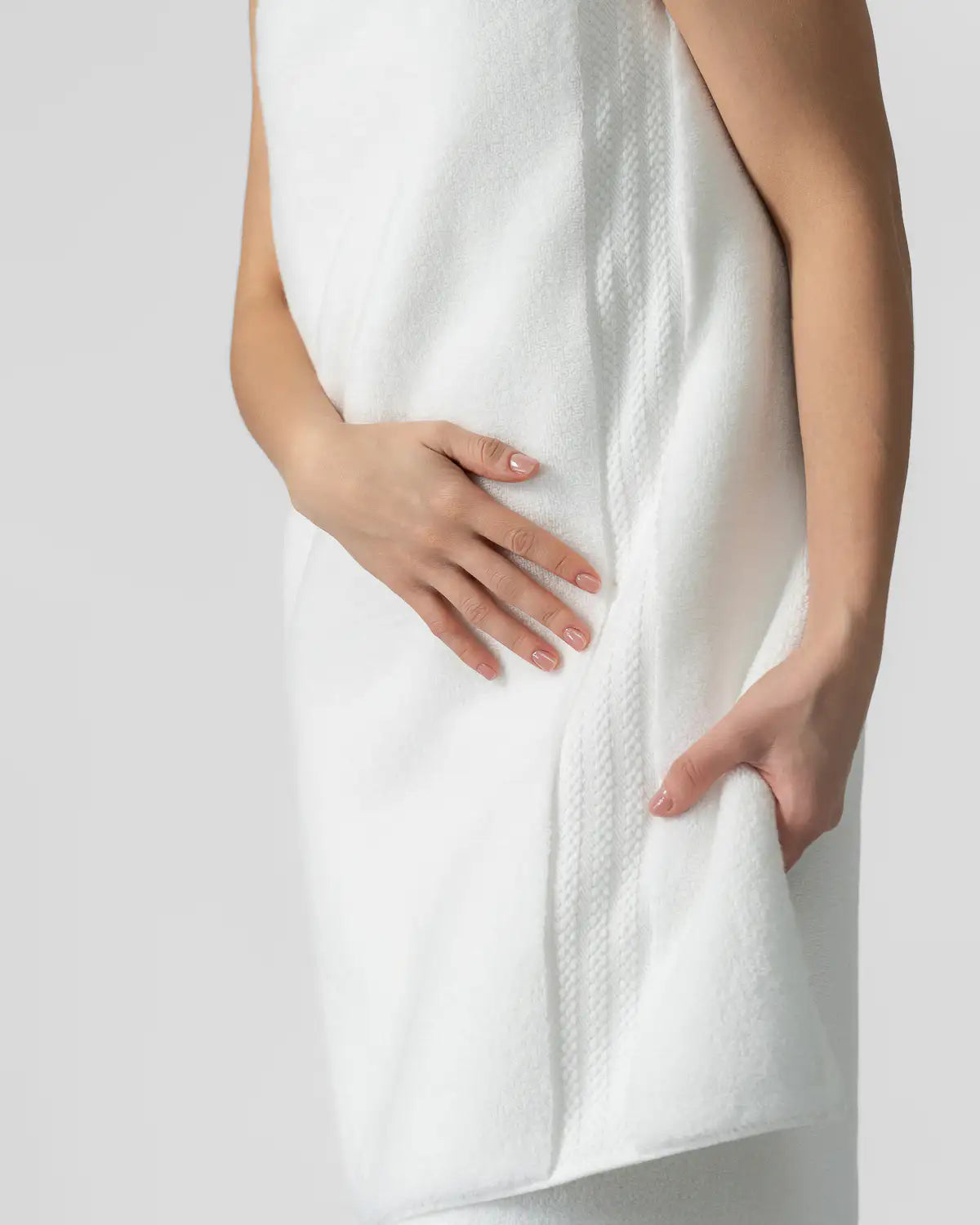 Person draped in white plush towels against a light gray background